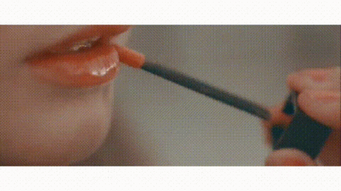 A Woman Is Applying Lip Gloss With A Brush To Her Lips . GIF