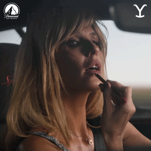 A Woman Is Applying Lipstick In A Car With A Paramount Network Logo GIF