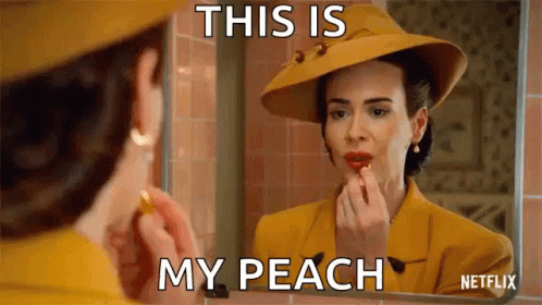 A Woman Is Applying Lipstick In Front Of A Mirror While Wearing A Yellow Hat . GIF