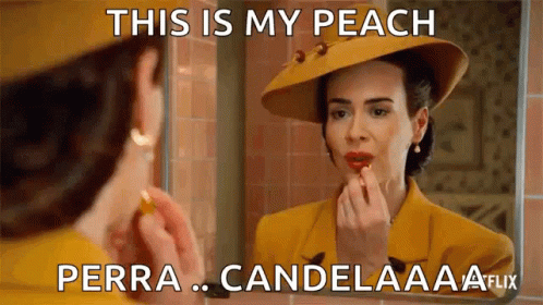 A Woman Is Applying Lipstick In Front Of A Mirror While Wearing A Yellow Suit And Hat . GIF