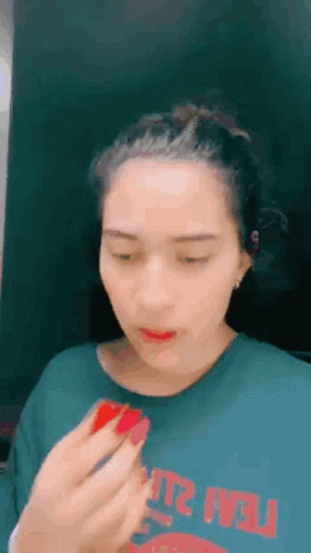 a woman is applying lipstick to her lips while wearing a green t-shirt .