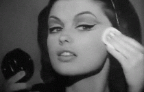 A Woman Is Applying Makeup To Her Face With A Sponge . GIF