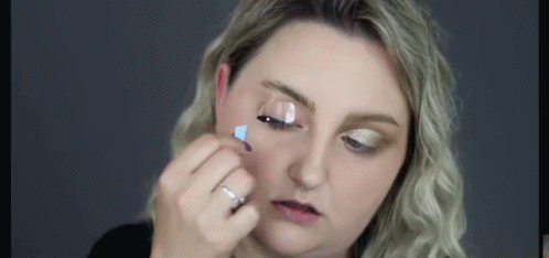 A Woman Is Applying Mascara To Her Eyelashes With A Brush . GIF