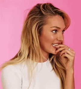 A Woman Is Biting Her Finger While Wearing A White Shirt . GIF