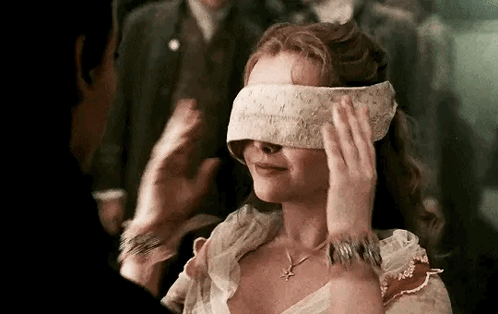 A Woman Is Blindfolded And Smiling While A Man Holds Her Hand Over Her Eyes . GIF