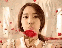 A Woman Is Blowing A Kiss While Holding A Red Rose . GIF