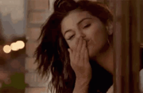 A Woman Is Blowing A Kiss While Standing Next To A Window . GIF