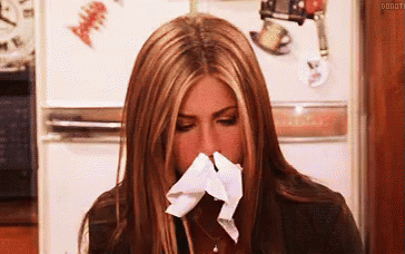 A Woman Is Blowing Her Nose With A Napkin While Sitting In Front Of A Refrigerator . GIF