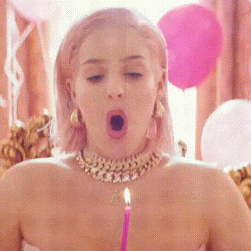 A Woman Is Blowing Out A Birthday Candle In A Room With Pink Balloons . GIF