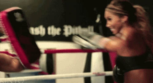 A Woman Is Boxing In A Ring With A Sign Behind Her That Says " Ash The Dust " GIF