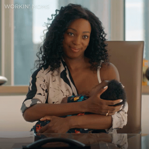 A Woman Is Breastfeeding A Baby While Sitting At A Desk GIF