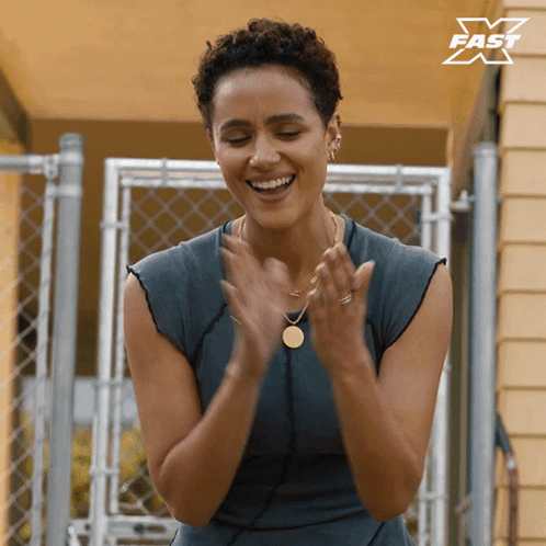 A Woman Is Clapping Her Hands In Front Of A Fence With A X Fast Logo In The Corner GIF