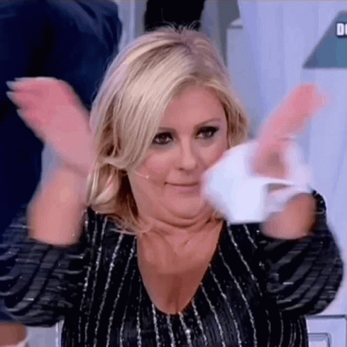 A Woman Is Clapping Her Hands In The Air While Wearing A Black And Silver Striped Shirt . GIF