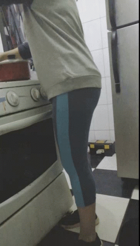 A Woman Is Cooking On A Stove In A Kitchen With A Refrigerator In The Background GIF