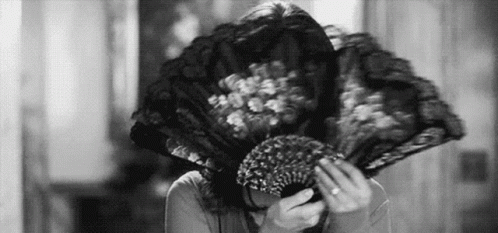 A Woman Is Covering Her Face With A Fan . GIF