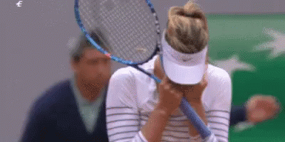 A Woman Is Covering Her Face With A Tennis Racket . GIF