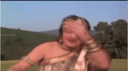 A Woman Is Covering Her Face With Her Hand While Dancing In A Field . GIF
