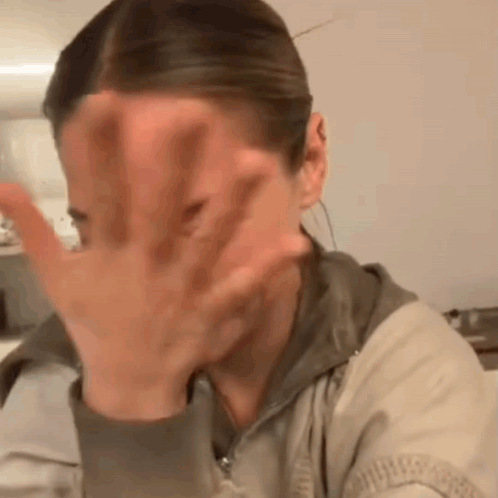 a woman is covering her face with her hand while sitting at a table .
