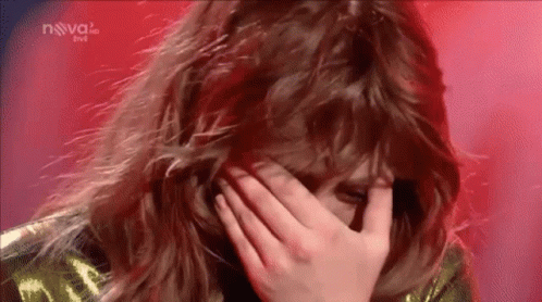A Woman Is Covering Her Face With Her Hand While Standing On A Stage . GIF