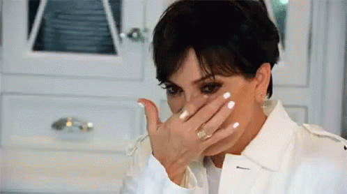 A Woman Is Covering Her Face With Her Hand While Wearing A White Jacket . GIF