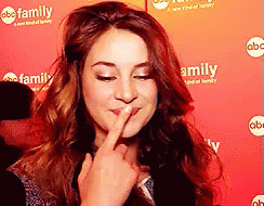 A Woman Is Covering Her Mouth With Her Finger In Front Of A Red Background That Says Family GIF