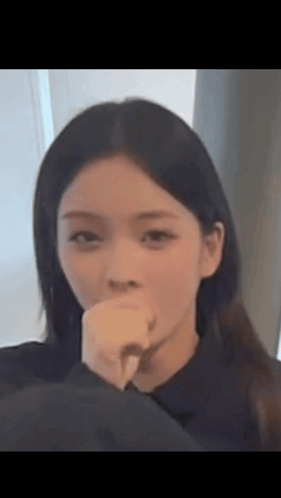 A Woman Is Covering Her Mouth With Her Hand And Looking At The Camera . GIF