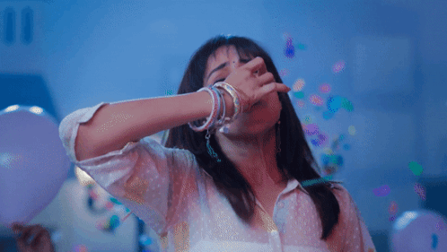 A Woman Is Covering Her Mouth With Her Hand While Confetti Falls Around Her GIF