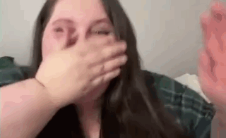 A Woman Is Covering Her Mouth With Her Hand While Laying On A Bed . GIF