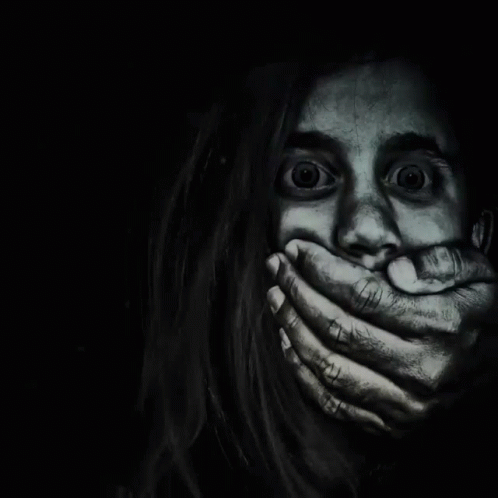 A Woman Is Covering Her Mouth With Her Hands In The Dark GIF