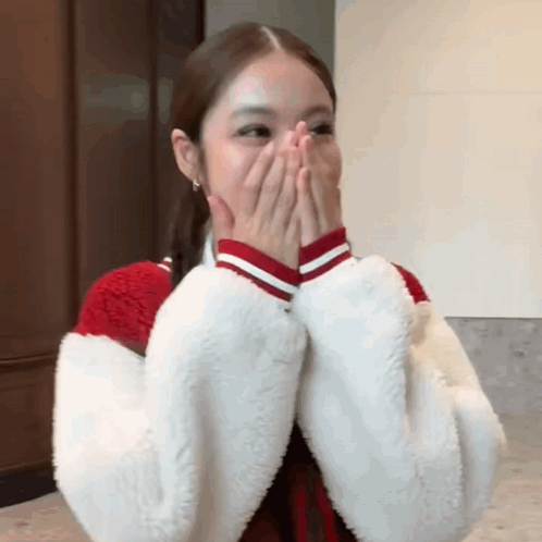 A Woman Is Covering Her Mouth With Her Hands While Wearing A Red And White Jacket . GIF