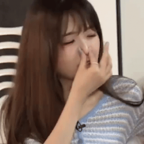 A Woman Is Covering Her Nose With Her Hand While Wearing A Blue Sweater . GIF