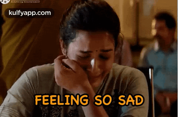 A Woman Is Crying While Sitting At A Table With The Words `` Feeling So Sad '' Written Above Her . GIF