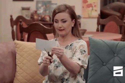 A Woman Is Cutting A Piece Of Paper With Scissors . GIF