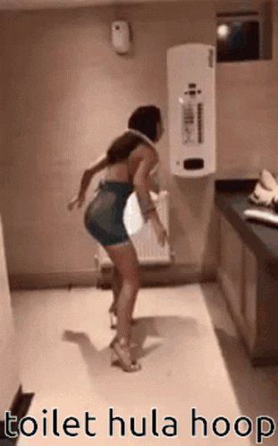 A Woman Is Dancing In A Bathroom With A Toilet Hula Hoop Around Her Waist . GIF