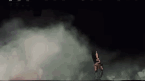A Woman Is Dancing In A Dark Room With Smoke Coming Out Of The Walls . GIF