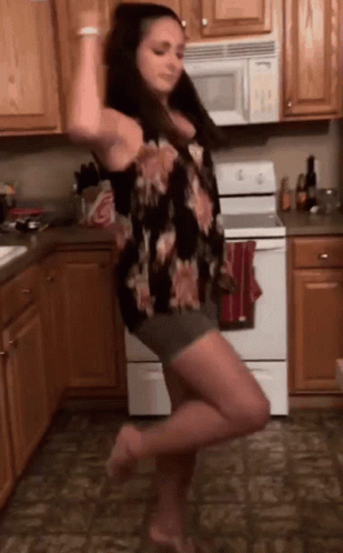 A Woman Is Dancing In A Kitchen In Front Of A Stove . GIF