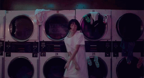 A Woman Is Dancing In A Laundromat With A Sign That Says Tank Queen On It GIF