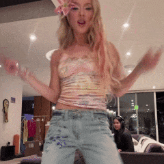 A Woman Is Dancing In A Living Room With A Flower In Her Hair GIF