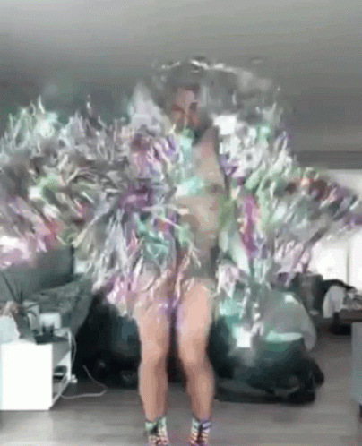 A Woman Is Dancing In A Room Wearing A Feathered Dress . GIF