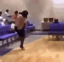 A Woman Is Dancing In A Waiting Room In Front Of Purple Benches . GIF