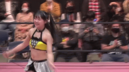 a woman is dancing in a wrestling ring in front of a crowd of people .