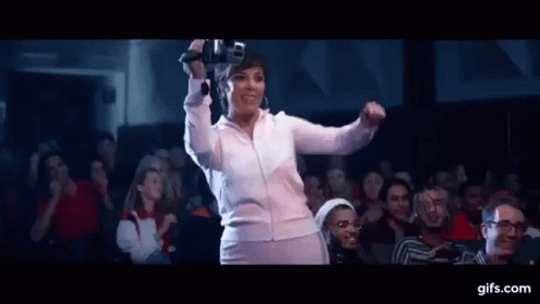 A Woman Is Dancing In Front Of A Crowd Of People In A Theater While Holding A Microphone . GIF