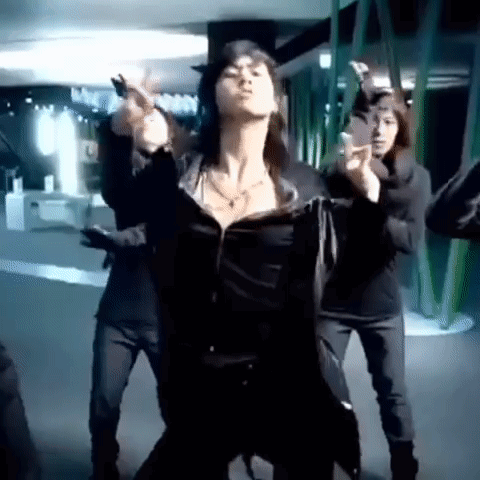 A Woman Is Dancing In Front Of A Group Of People In A Dark Room . GIF