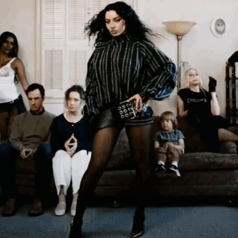 A Woman Is Dancing In Front Of A Group Of People Who Are Sitting On A Couch GIF