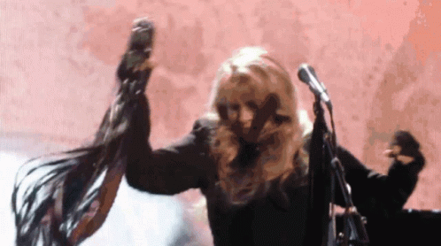 A Woman Is Dancing In Front Of A Microphone While Her Hair Blows In The Wind . GIF
