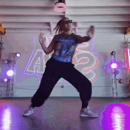 A Woman Is Dancing In Front Of A Wall That Has The Letter A On It GIF