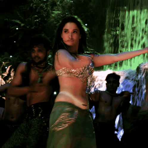 A Woman Is Dancing In Front Of A Waterfall In A Green Light GIF