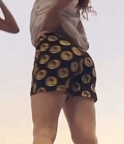 A Woman Is Dancing On A Beach Wearing Shorts With Circles On Them . GIF