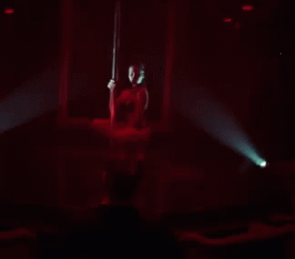 A Woman Is Dancing On A Pole In A Dark Room GIF