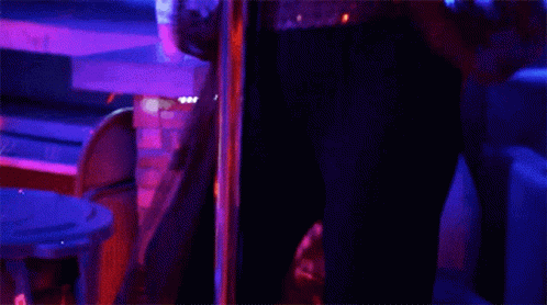 A Woman Is Dancing On A Pole In A Dark Room With Glow In The Dark Bracelets On Her Wrists . GIF